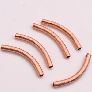 May include: Five rose gold colored metal connector pieces for jewelry making. Each piece is a curved tube with a textured surface.