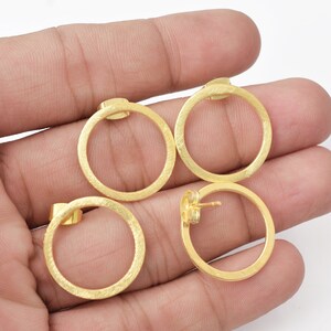 May include: A pair of gold-toned hoop earrings with a textured finish. The earrings are circular and have a slightly hammered look.