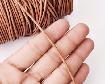 May include: Close-up of a brown leather cord, showing its texture and flexibility. The cord is held in a hand, demonstrating its thickness and strength.