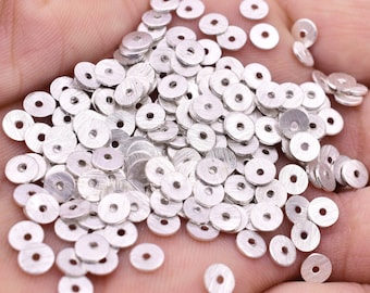 May include: A large pile of silver-coloured metal jump rings. The rings are all the same size and shape, and they are arranged in a random pattern.