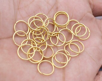May include: A pile of gold-colored jump rings, also known as split rings, are shown on a hand. These rings are used for jewelry making and crafting.