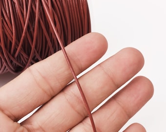 May include: Close-up of a reel of brown leather cord. A single strand of the cord is stretched out across a hand.