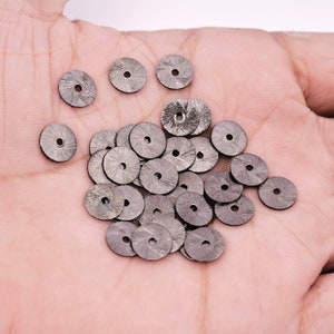 Könnte beinhalten: Ein Haufen silberfarbener Metallpailletten mit einer strukturierten Oberfläche. Die Pailletten sind rund mit einem kleinen Loch in der Mitte.