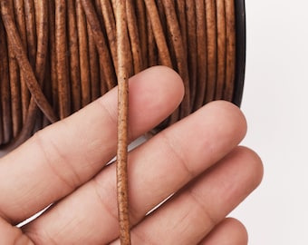 May include: Close-up of a spool of brown leather cord. A single strand of the cord is held in a hand, showing the texture and thickness of the cord.