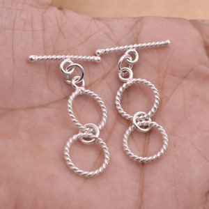 May include: Two silver toggle clasps with a double circle design. Each clasp has a twisted bar and a dangling double circle charm.