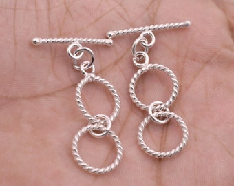 May include: Two silver toggle clasps with a double circle design. Each clasp has a twisted bar and a dangling double circle charm.