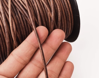 May include: A spool of brown leather cord, with a length of cord being held in a hand.