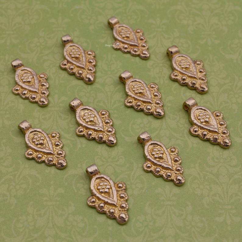 Pu&ograve; includere: Dieci ciondoli pendenti in metallo dorato con forma a goccia e dettagli intricati di perline. I ciondoli hanno una superficie leggermente testurizzata e un anello nella parte superiore per il fissaggio a gioielli.