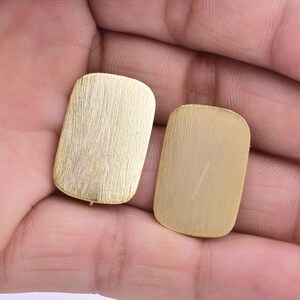 Puede incluir: Dos pendientes rectangulares de color dorado con acabado cepillado.