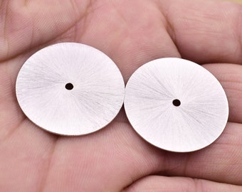May include: Two silver watch dials with a sunburst pattern and a small hole in the centre.