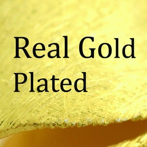 May include: Close-up of a gold-colored surface with the words "Real Gold Plated" in black text. The surface has a textured appearance, with visible brushstrokes and a slightly rough texture.