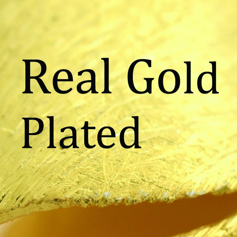 May include: Close-up of a gold-colored surface with the words "Real Gold Plated" in black text. The surface has a textured appearance, with visible brushstrokes and a slightly rough texture.