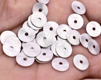 May include: A pile of silver metal round beads with a textured surface and a hole in the centre. The beads are approximately 2.5 cm in diameter.