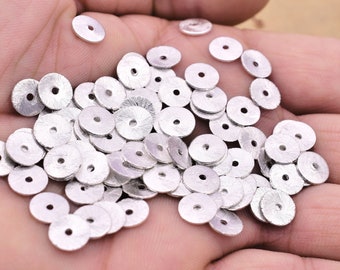 May include: A pile of silver-coloured metal round beads with a hole in the centre. The beads have a textured surface.
