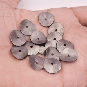 May include: A collection of silver-toned metal buttons with a circular shape and a small hole in the centre. The buttons have a textured, slightly raised surface.