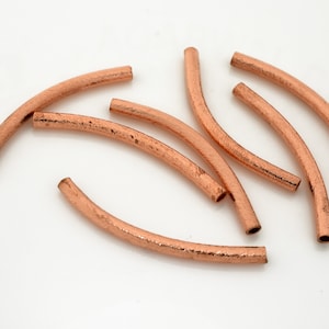 May include: A group of seven copper-colored metal beads, each with a slightly curved shape and a textured surface.