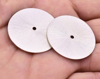 May include: Two silver watch dials with a sunburst pattern and a small hole in the centre.