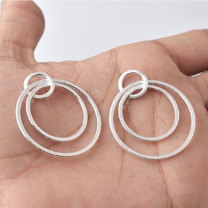 May include: A pair of silver hoop earrings with a double circle design. The earrings have a textured finish and are a simple and elegant style.