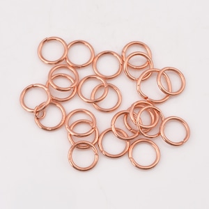 Puede incluir: Un grupo de 18 anillos de salto de oro rosa. Los anillos de salto son pequeños y redondos, y son perfectos para la elaboración de joyas.