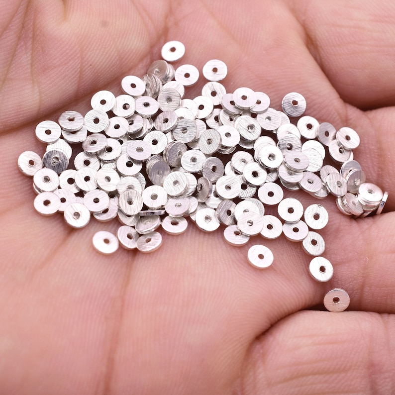 May include: A large pile of silver-colored metal spacer beads. The beads are round with a hole in the center.