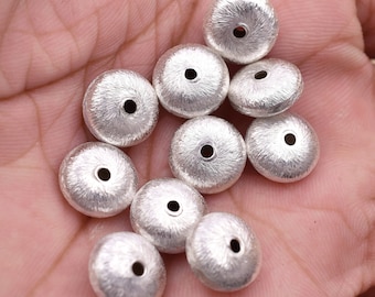 May include: A collection of ten silver-toned metal beads with a textured surface. The beads are round with a hole in the center.