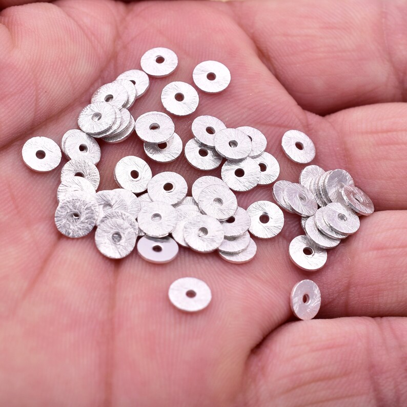 May include: A pile of silver-colored metal round beads with a textured surface.