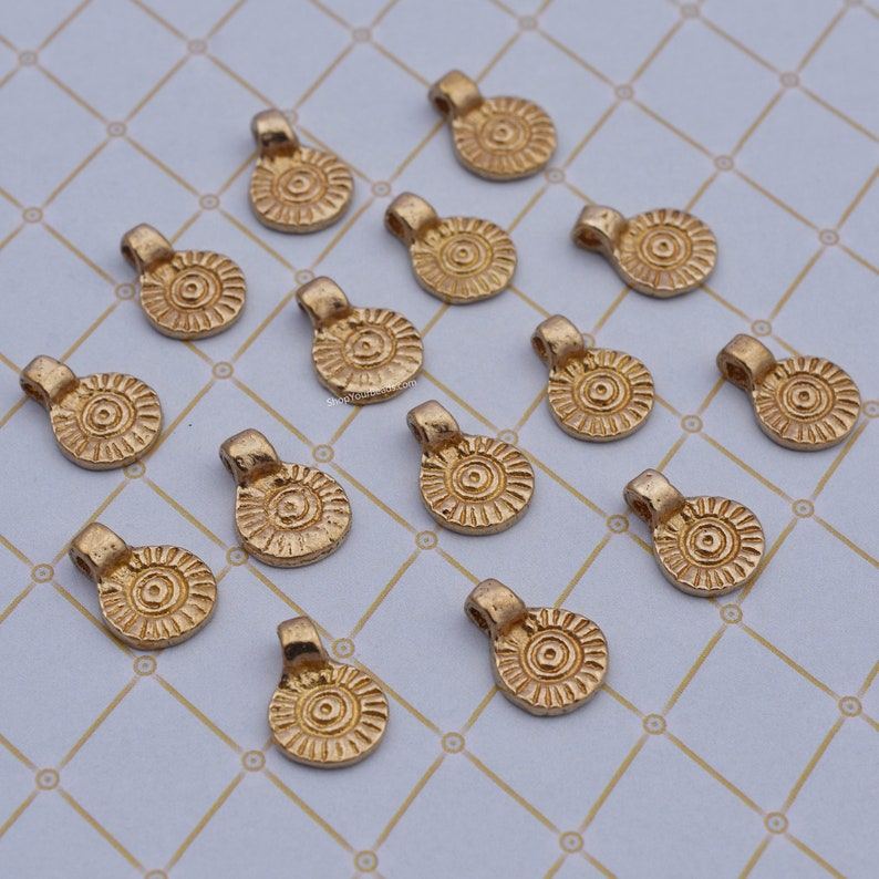 May include: A collection of 15 gold-toned metal pendant charms with a circular design. Each charm has a raised, textured centre and a loop at the top for attaching to jewellery.