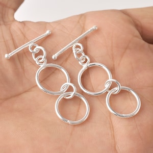 May include: Two silver toggle clasps with double ring accents. Each clasp features a silver bar with a round end and a silver chain connecting to two interlocking rings.