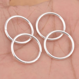 May include: Four silver jump rings, each with a smooth, circular shape. The rings are arranged in a loose cluster on a hand.