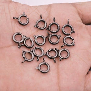 May include: A close-up of a pile of 15 silver-toned metal lobster clasps. The clasps are round and have a spring-loaded mechanism.