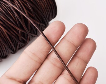 May include: Close-up of a spool of dark brown leather cord. A strand of the cord is held in a hand, showing its texture and color. The cord appears to be tightly wound and ready for use in crafting projects.