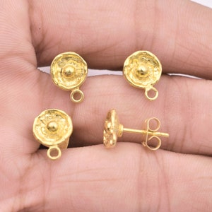 May include: Four gold-colored earring components. Each component has a textured, circular design with a small, raised center and a loop for attachment. One earring is a stud with a post.