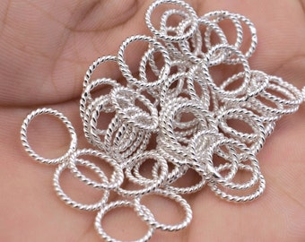 May include: A pile of silver-toned twisted wire rings. The rings are all the same size and are arranged in a random pattern.