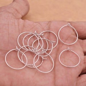 Pode incluir: Uma coleção de pequenos achados de brincos de argola prateados. Os aros são redondos com um pequeno laço na parte superior para fixar aos ganchos. Os achados são exibidos em um fundo neutro.