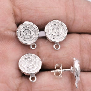 May include: Silver spiral earring findings with a loop for attaching a dangle charm. The findings are shown on a hand.