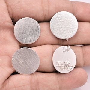 May include: Four silver round earring blanks with a brushed finish. Two blanks have earring posts attached to the back.