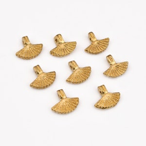 May include: Eight gold-colored metal fan-shaped charms with a loop at the top. The charms are arranged in a scattered pattern on a white background.