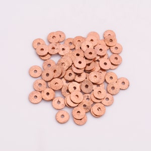 May include: A pile of copper-colored metal beads, each with a flat, round shape and a small hole in the center.