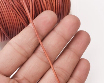 May include: Close-up of a reel of brown leather cord. The cord is thin and smooth, and it is being held in a person's hand.