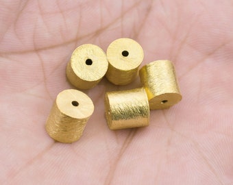 May include: Five gold-colored metal beads with a hole in the center. The beads are cylindrical and have a textured surface.