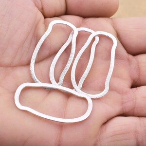 Puede incluir: Tres anillos de metal de color plateado, cada uno con una forma ligeramente diferente, están dispuestos en una pila sobre una mano.