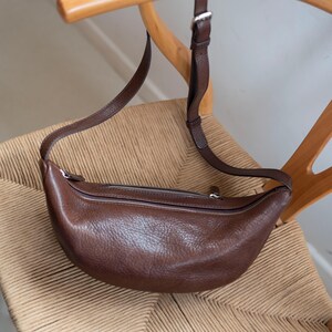 Chocolate full grain leather banana bag on wicker chair, moon shape vegetable tanned handmade crossbody sling bag product shot warm tones