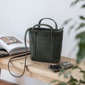 Forest green full grain leather crossbody bag with adjustable strap on desk