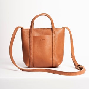 Tan full grain leather crossbody bag with adjustable strap on white background