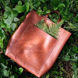 Brown copper full grain leather tote backpack on green leaves, handmade vegetable tanned leather bag