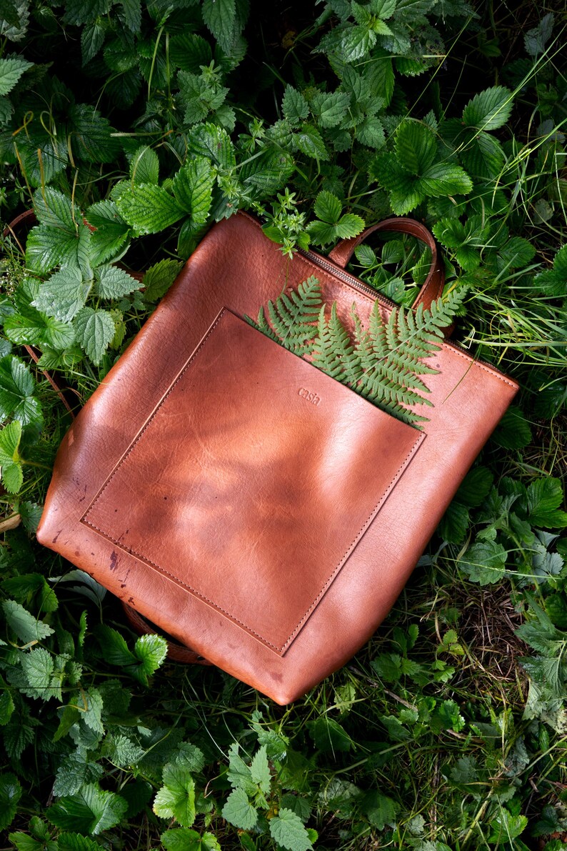 Brown copper full grain leather tote backpack on green leaves, handmade vegetable tanned leather bag