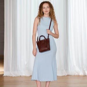 Young woman carrying bordeaux leather bag by top handle with blue dress