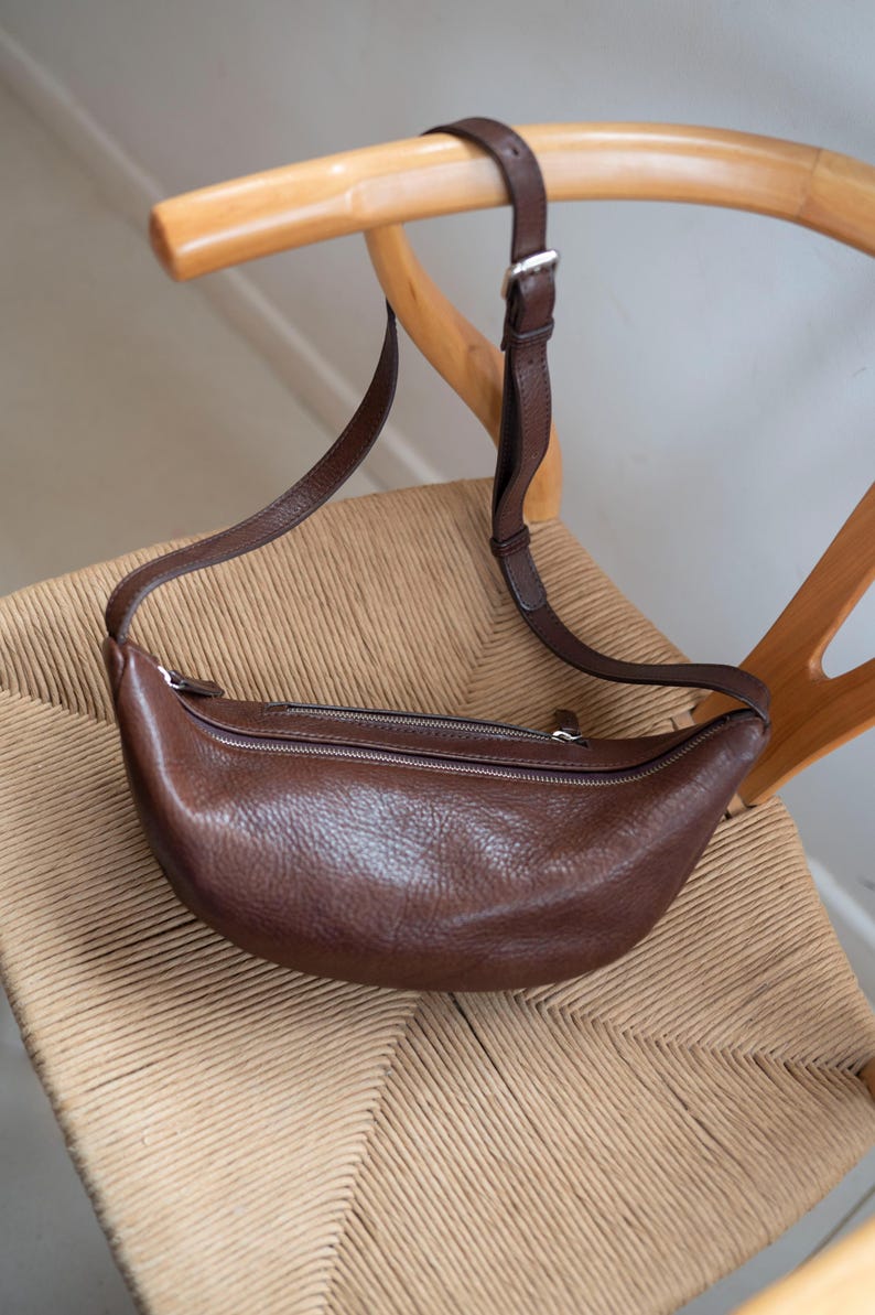 Chocolate full grain leather banana bag on wicker chair, moon shape vegetable tanned handmade crossbody sling bag product shot warm tones
