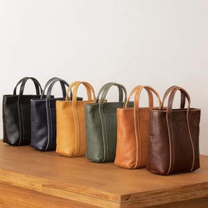 Six color options of handmade leather tote bag displayed on wooden surface