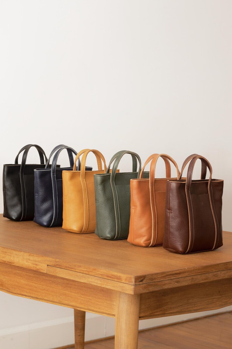 Six color options of handmade leather tote bag displayed on wooden surface